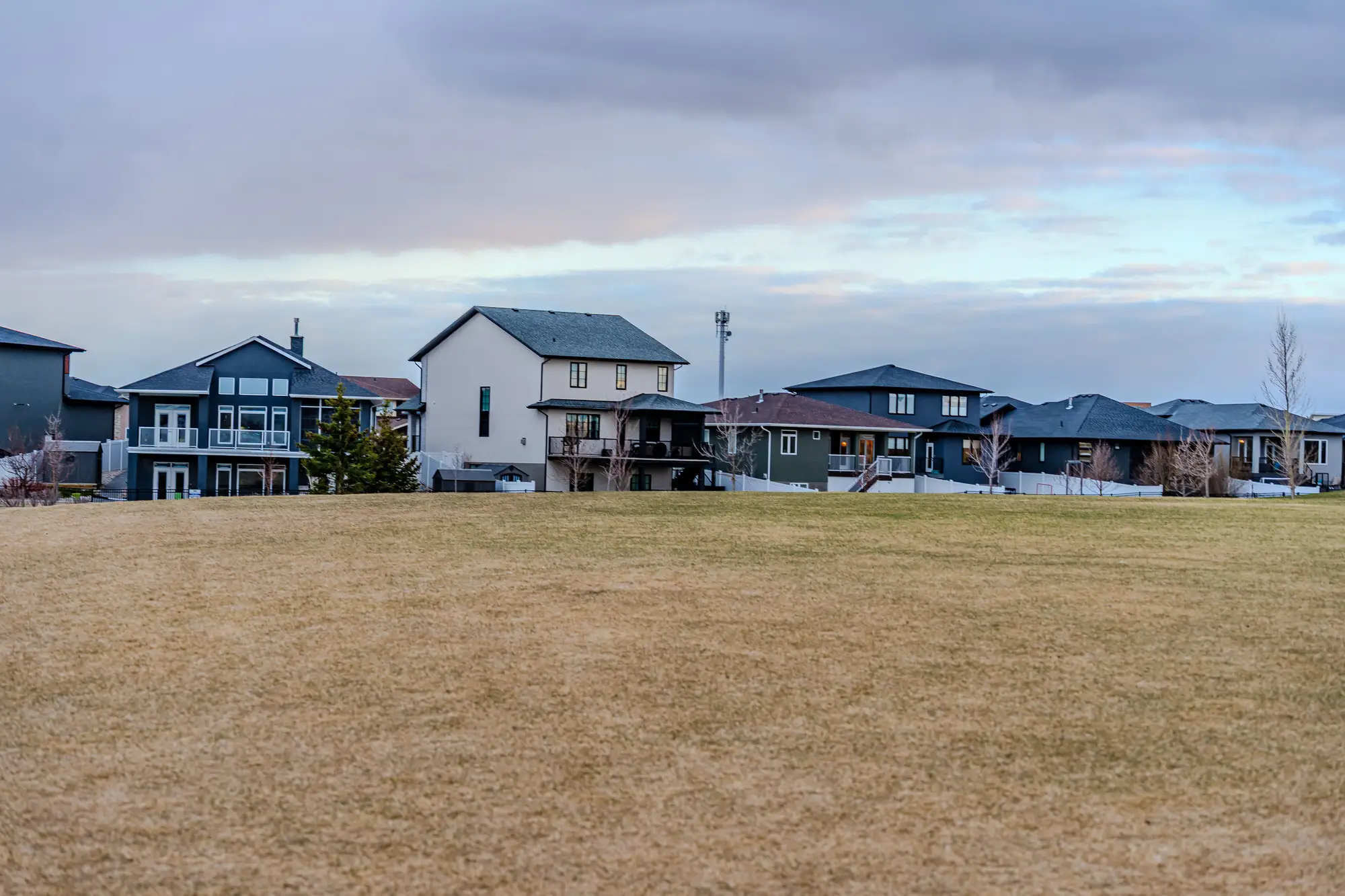 Two-storey houses along the edge of a grass field under an overcast sky